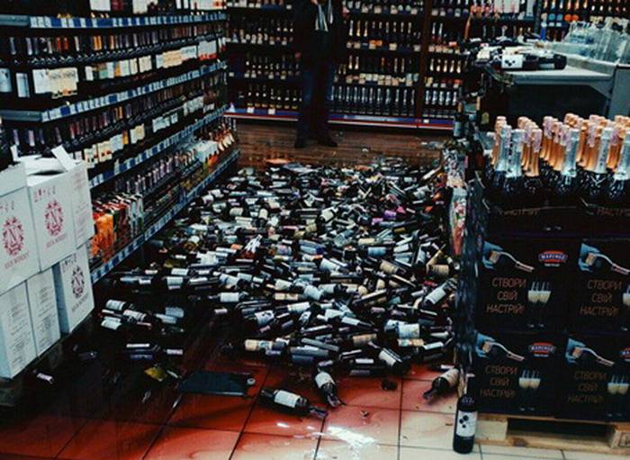 Разбитые бутылки в магазине. Стеллаж с бутылками вина в магазине.